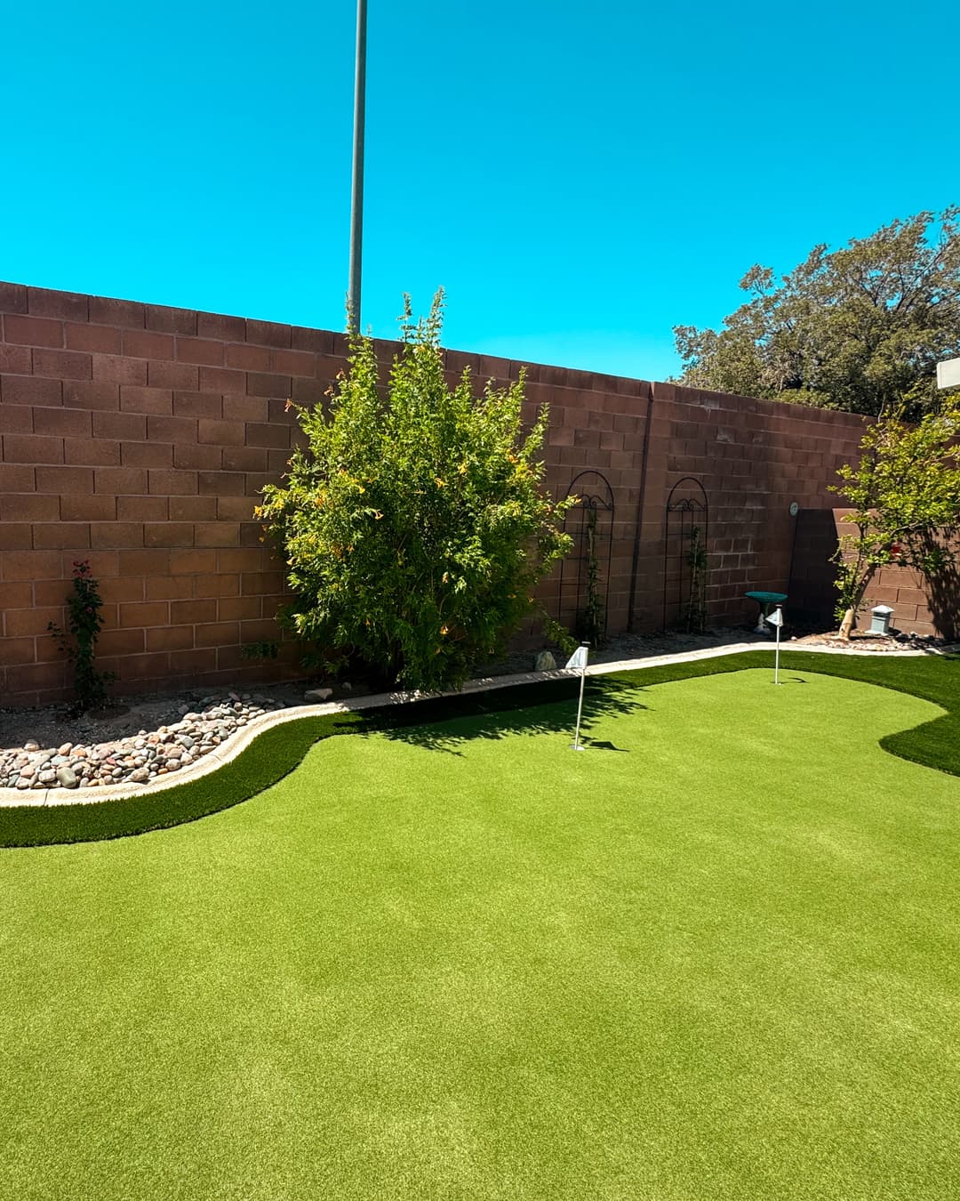 Lush green artificial grass landscape with garden features and clear blue sky.