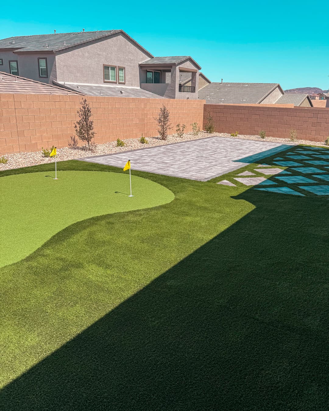 Backyard golf putting green with flags, landscaped stones, and modern home architecture.