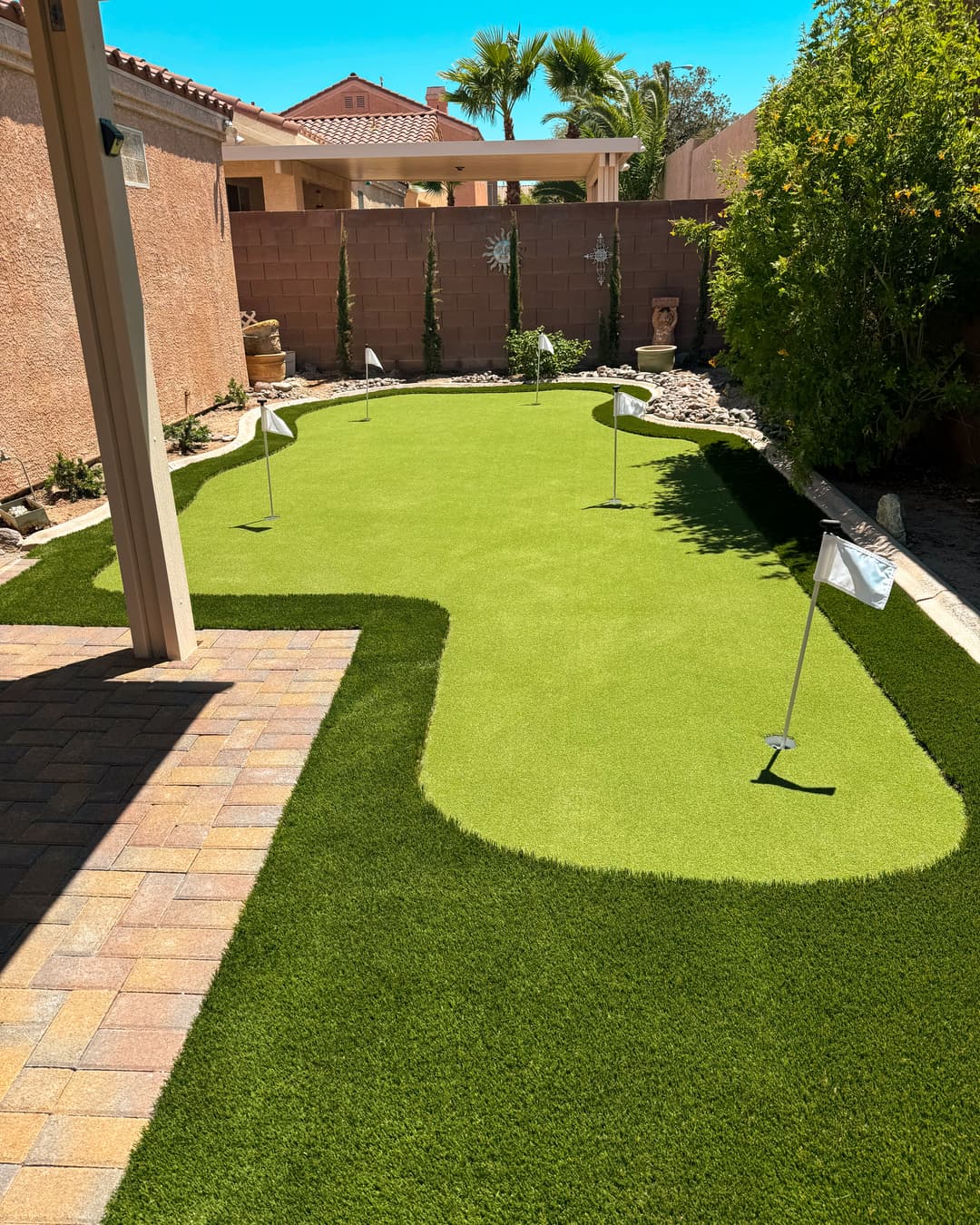 Backyard putting green with four flags, surrounded by landscape and patio area.