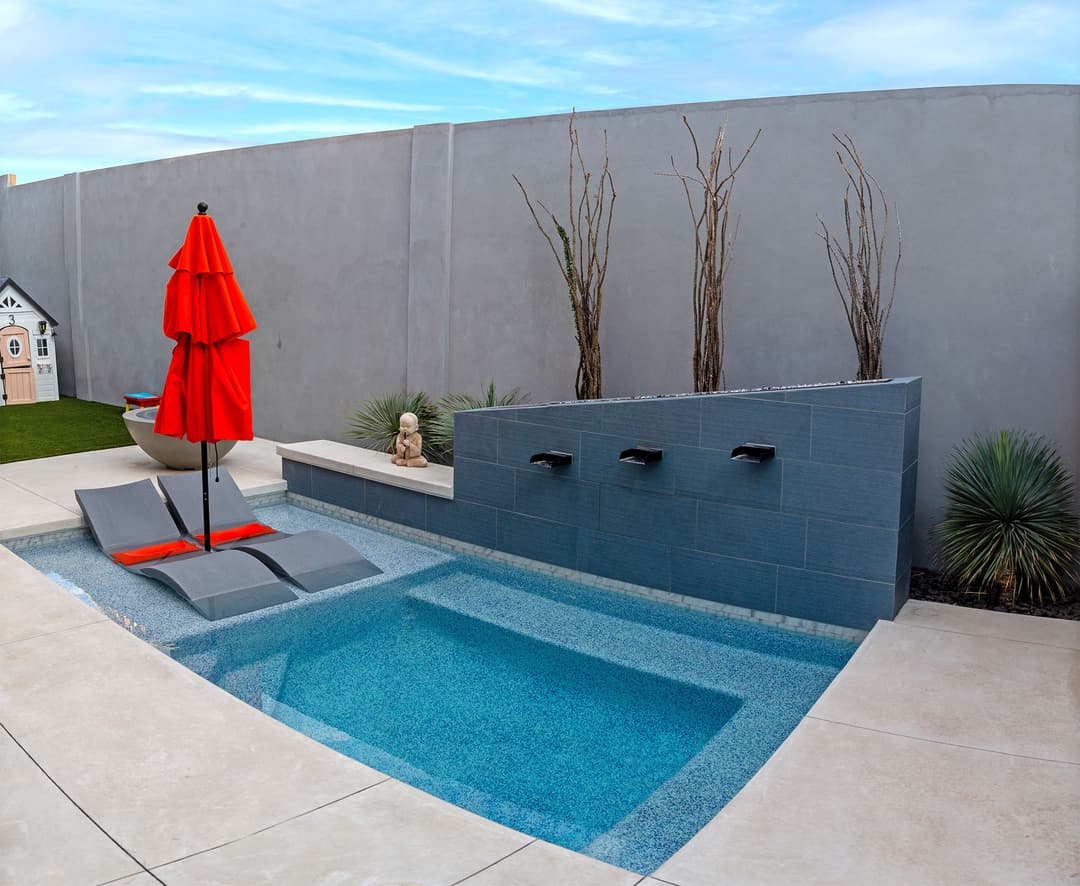 Modern backyard oasis with a small pool, lounge chairs, red umbrella, and decorative planters.
